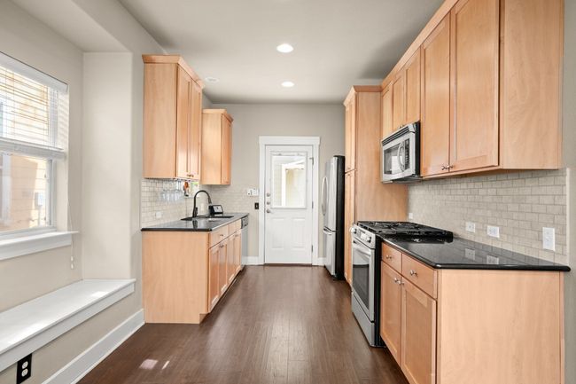 Kitchen with baseboards, light brown cabinetry, dark wood finished floors, stainless steel appliances, and a sink | Image 10