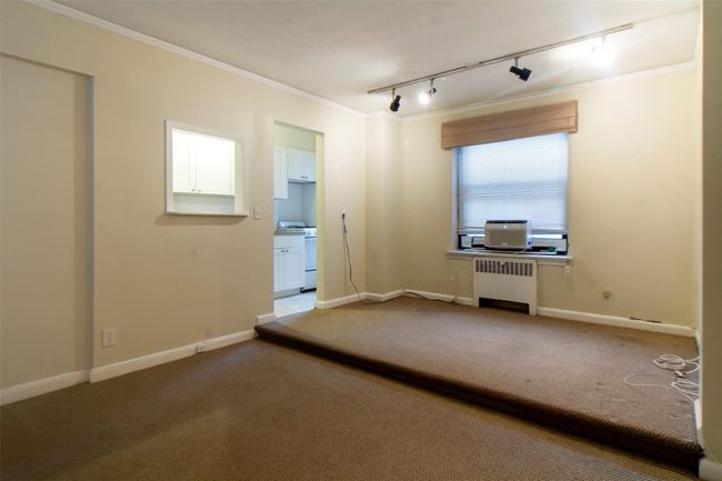 Carpeted empty room featuring crown molding, rail lighting, and radiator heating unit | Image 4