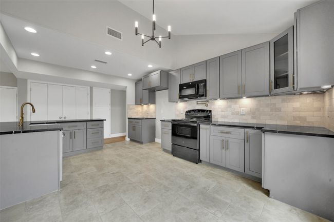 Kitchen with black appliances, gray cabinetry, dark countertops, backsplash, and vaulted ceiling | Image 8
