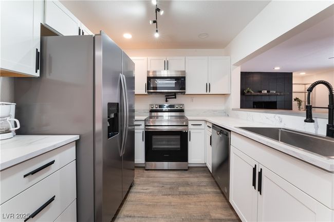 Kitchen with white cabinetry, a sink, appliances with stainless steel finishes, and wood finished floors | Image 12