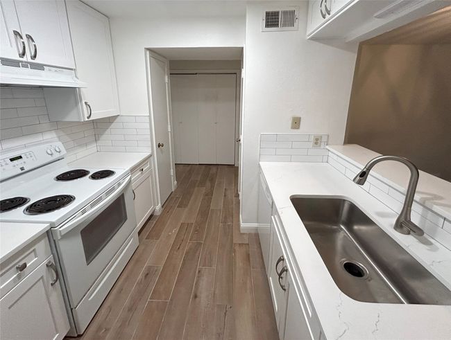 Kitchen featuring large stainless-steel sink, white cabinetry, Luxury Vinyl Plank flooring, white range with electric stovetop, and backsplash | Image 14