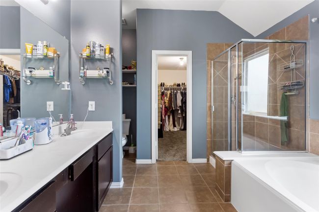 This bathroom features a double vanity with ample counter space, a glass-enclosed shower, a separate bathtub, and access to a spacious walk-in closet. | Image 7
