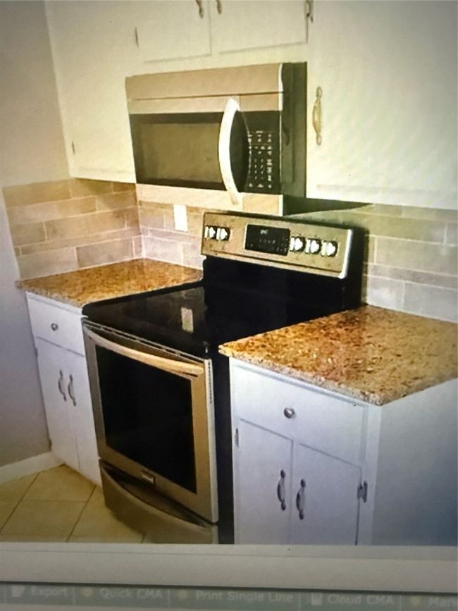 Kitchen featuring stainless steel range with electric cooktop, backsplash, light tile patterned floors, light stone countertops, and white cabinets | Image 12