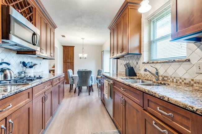 Kitchen featuring a sink, appliances with stainless steel finishes, a chandelier, light wood-style flooring, and brown cabinetry | Image 7