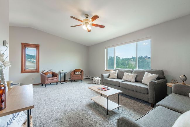 Living room with ceiling fan, lofted ceiling, carpet flooring, and a baseboard heating unit | Image 4