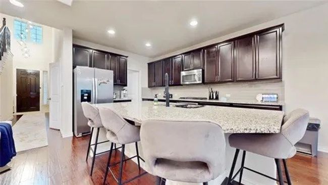 Kitchen with appliances with stainless steel finishes, a breakfast bar area, light stone countertops, dark wood-type flooring, and dark brown cabinetry | Image 16
