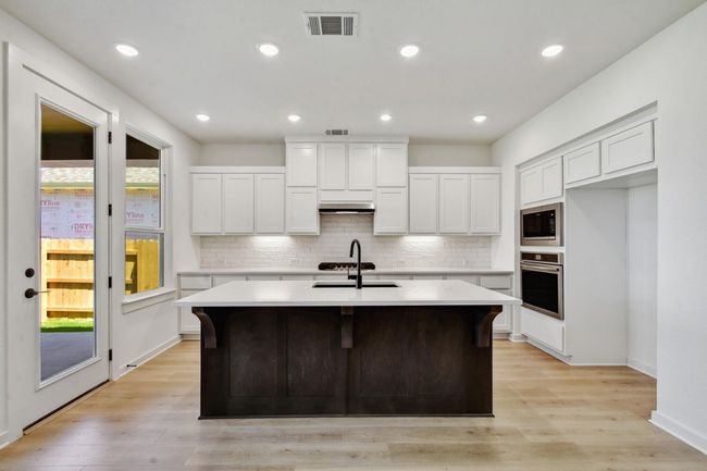 Kitchen featuring white cabinets, light wood-style floors, a kitchen breakfast bar, decorative backsplash, and recessed lighting | Image 7