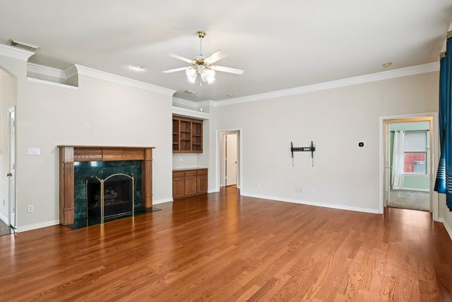 Unfurnished living room with ornamental molding, wood finished floors, a fireplace, and ceiling fan | Image 4