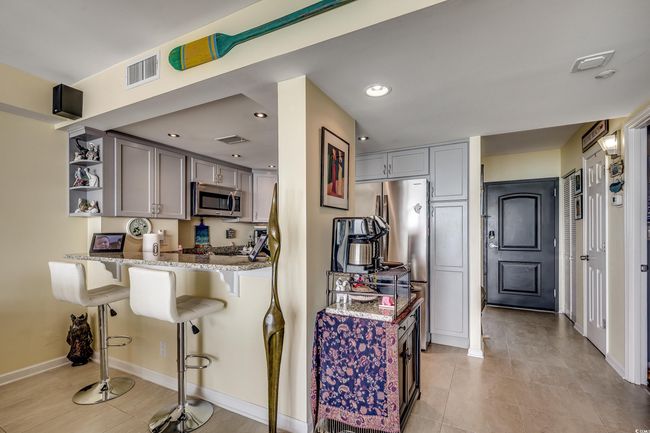 Kitchen featuring appliances with stainless steel finishes, open shelves, light stone countertops, a kitchen bar, and gray cabinetry | Image 6