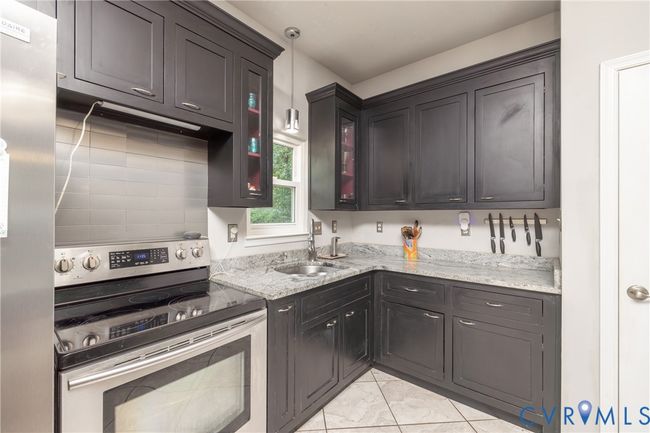 Kitchen with appliances with stainless steel finishes, light stone countertops, glass insert cabinets, pendant lighting, and light tile patterned floors | Image 36