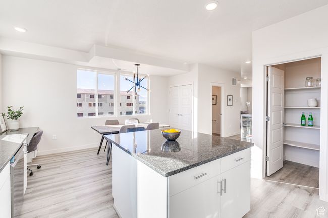 Kitchen with light wood-style flooring, a chandelier, white cabinets, pendant lighting, and dark stone countertops | Image 11