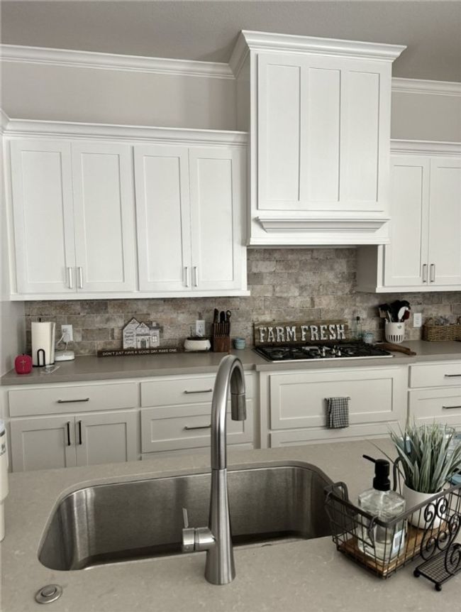 Kitchen with stainless steel gas stovetop, ornamental molding, white cabinetry, backsplash, and light countertops | Image 8