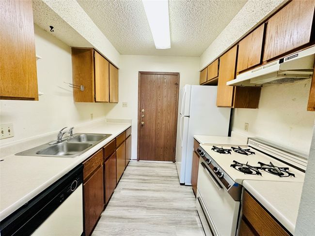Kitchen featuring white appliances, light countertops, light wood-style floors, under cabinet range hood, and a textured ceiling | Image 9