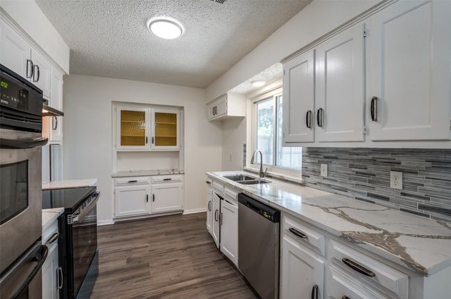 Kitchen with stainless steel appliances, a textured ceiling, tasteful backsplash, dark wood-type flooring, and white cabinetry | Image 9