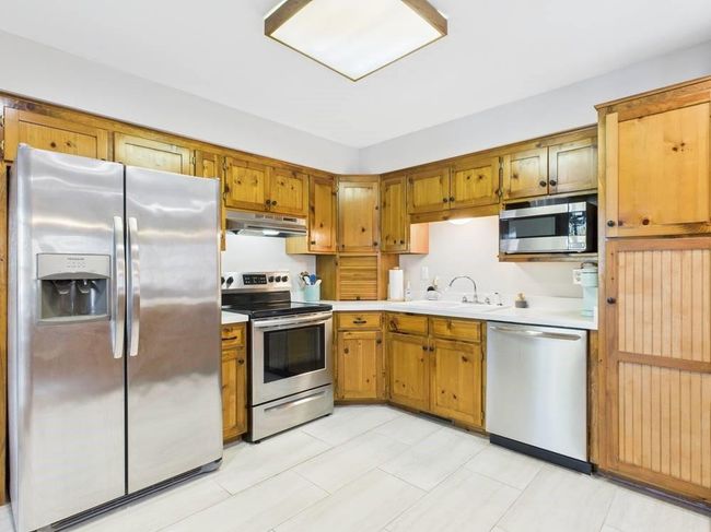 Kitchen with appliances with stainless steel finishes, under cabinet range hood, light countertops, a sink, and wood cabinets | Image 37