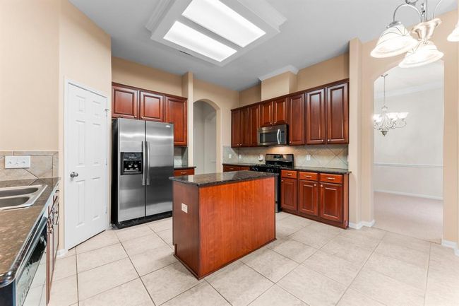This well-appointed kitchen features rich wood cabinetry, granite countertops, stainless steel appliances, and a central island ideal for meal prep or casual dining. With an open layout, built-in desk, and easy access to the dining room, it's designed for both functionality and effortless entertaining. | Image 9