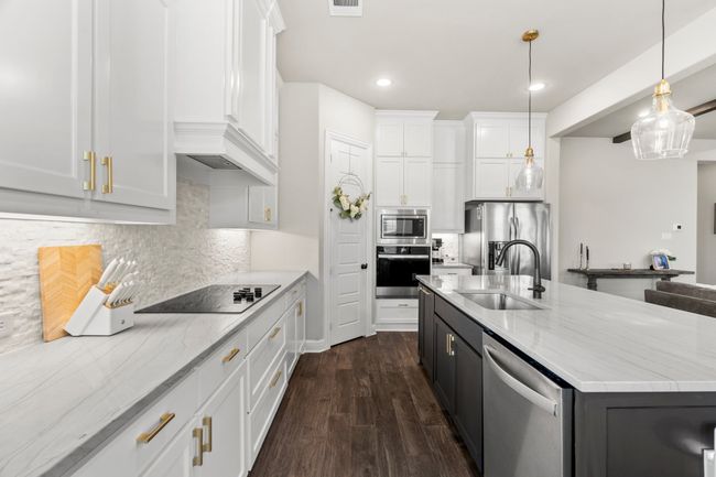 Kitchen featuring appliances with stainless steel finishes, white cabinets, tasteful backsplash, light stone counters, and a center island with sink | Image 12
