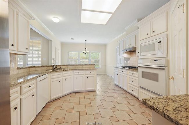 Kitchen with appliances with stainless steel finishes, a sink, tasteful backsplash, a peninsula, and white cabinetry | Image 5