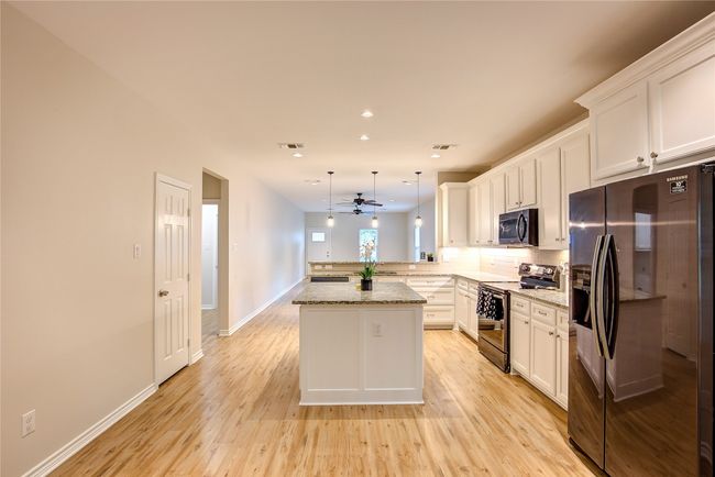 Kitchen with electric range, black fridge with ice dispenser, a peninsula, ceiling fan, and white cabinets | Image 12