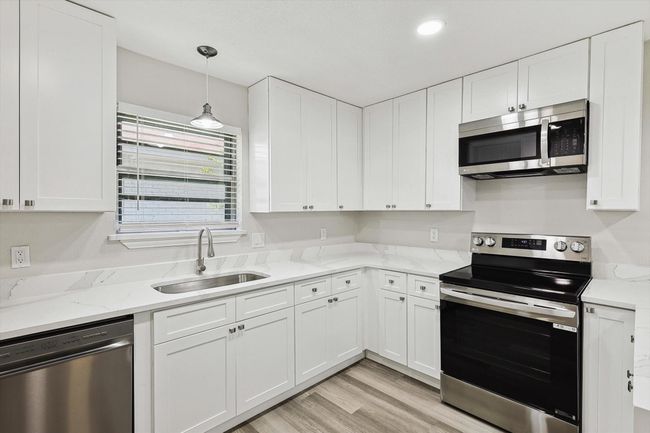 Kitchen with light wood-style flooring, white cabinets, a sink, stainless steel appliances, and light stone countertops | Image 9