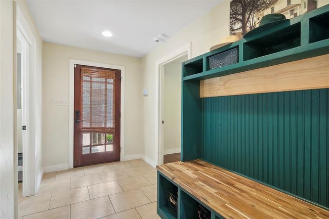 This entryway features a welcoming wooden front door with a bamboo shade, tiled flooring, and a built-in green bench with storage options, providing a functional and stylish space. | Image 23