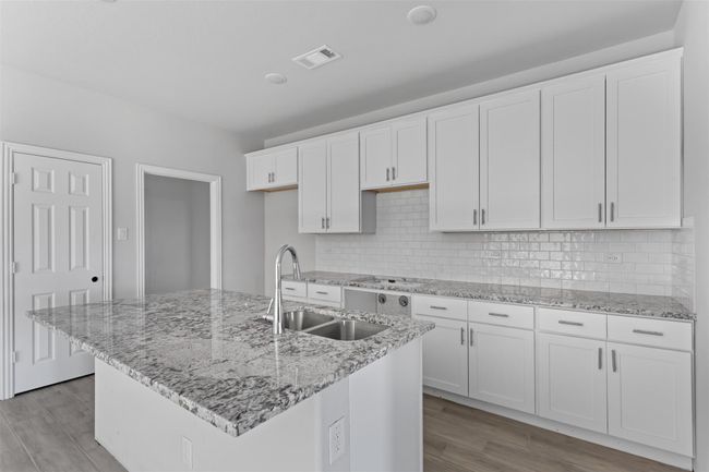 Kitchen featuring white cabinetry, light hardwood / wood-style flooring, a center island with sink, backsplash, and sink | Image 6