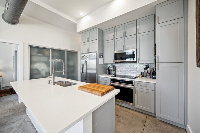 Kitchen featuring appliances with stainless steel finishes, gray cabinets, light countertops, decorative backsplash, and a kitchen island with sink | Image 10