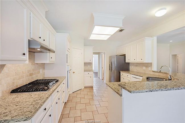 Kitchen featuring a sink, under cabinet range hood, stainless steel appliances, a peninsula, and decorative backsplash | Image 6