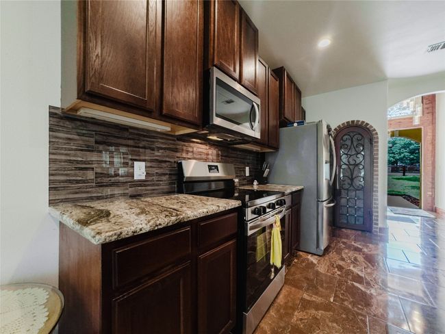 Kitchen featuring appliances with stainless steel finishes, arched walkways, dark brown cabinets, decorative backsplash, and light stone countertops | Image 12