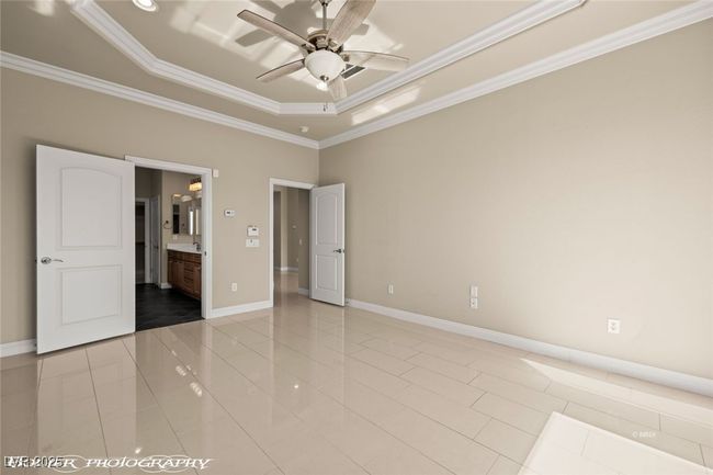Unfurnished bedroom featuring baseboards, light tile patterned floors, a tray ceiling, and crown molding | Image 41