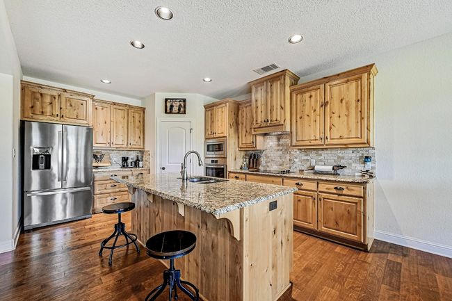 Kitchen with appliances with stainless steel finishes, dark wood-style floors, light stone countertops, a kitchen bar, and decorative backsplash | Image 10