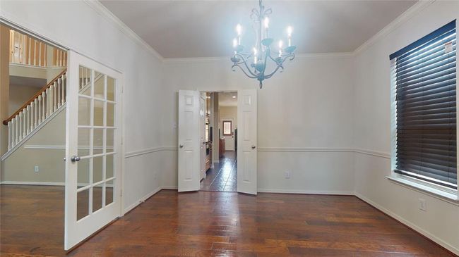 This room features hardwood flooring, a stylish chandelier, and ample natural light from a large window with blinds. French doors lead to a staircase, and there's an entryway to a kitchen area. | Image 8