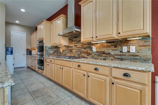 Kitchen featuring light brown cabinets, wall chimney range hood, stainless steel appliances, and tasteful backsplash | Image 24