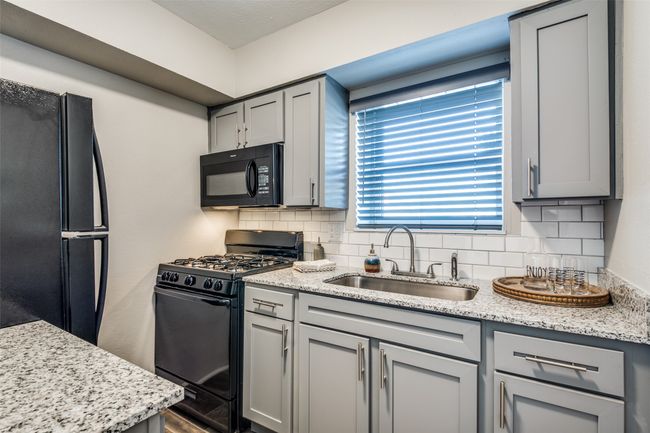 Kitchen with decorative backsplash, gray cabinetry, black appliances, and a sink | Image 7