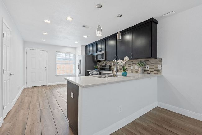 Kitchen featuring stainless steel appliances, light wood-style flooring, light countertops, tasteful backsplash, and a peninsula | Image 6