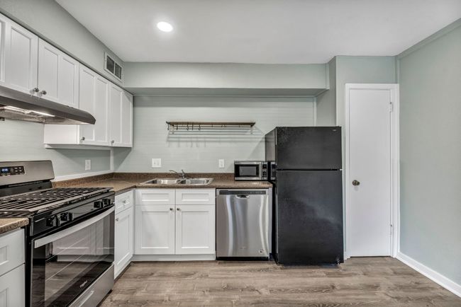 Kitchen with stainless steel appliances, a sink, under cabinet range hood, light wood-type flooring, and dark countertops | Image 5