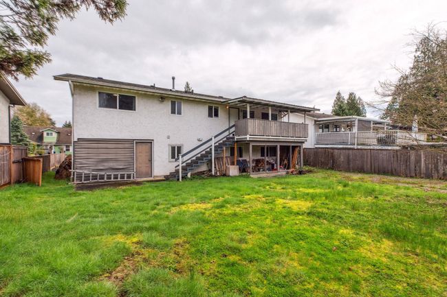 Rear view of house with a wooden deck, a fenced backyard, stucco siding, a lawn, and stairway | Image 39