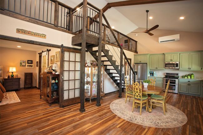 Dining area featuring high vaulted ceiling, a wall mounted air conditioner, a barn door, stairway, and dark wood-style flooring | Image 35