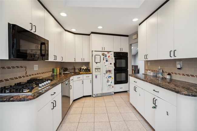 Kitchen featuring black appliances, tasteful backsplash, recessed lighting, white cabinets, and dark stone countertops | Image 6