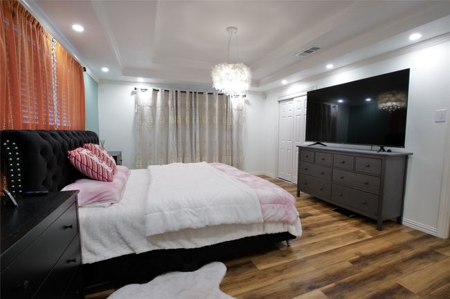 Bedroom featuring a raised ceiling, crown molding, a chandelier, wood finished floors, and recessed lighting | Image 17