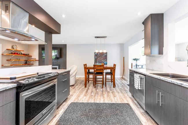 Kitchen featuring stainless steel appliances, wall chimney range hood, light wood-type flooring, light stone countertops, and modern cabinets | Image 10