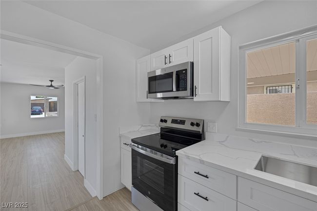 Kitchen featuring stainless steel appliances, light stone counters, white cabinetry, light wood-type flooring, and a ceiling fan | Image 12