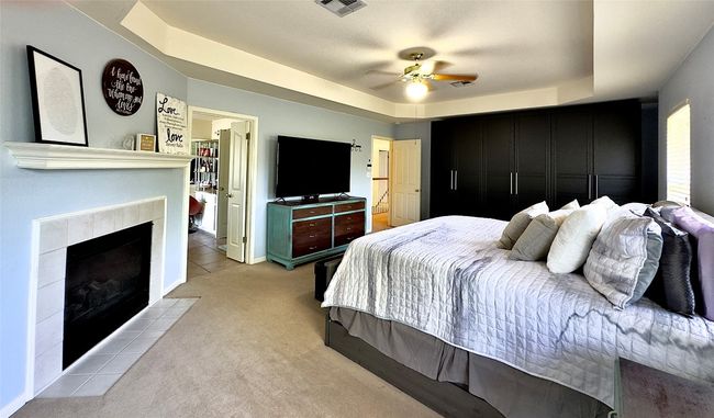 Master Bedroom featuring a tray ceiling, light colored carpet, a tiled fireplace, and a ceiling fan | Image 30