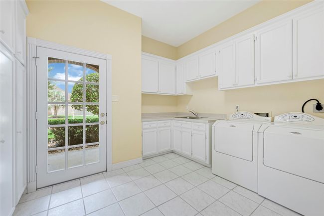 This pristine laundry room features ample cabinetry, a utility sink, spacious countertops, and room for an extra refrigerator. | Image 33