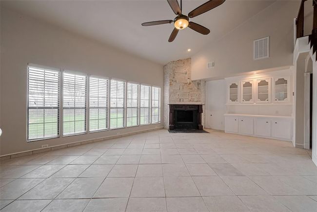 The spacious main living area boasts soaring ceilings, a dramatic wall of windows overlooking the backyard, and a statement stone fireplace. Built-in cabinetry adds character and storage, making this room the heart of the home. | Image 10