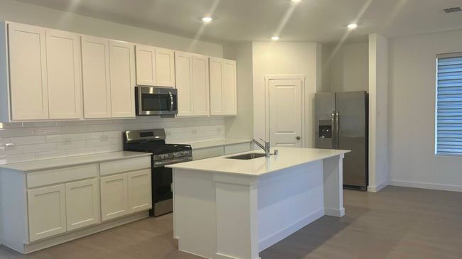 Kitchen with appliances with stainless steel finishes, white cabinets, decorative backsplash, a center island with sink, and light stone counters | Image 8