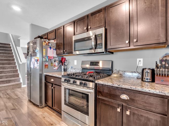 kitchen featuring appliances with stainless steel finishes, light wood-style floors, light stone counters, baseboards, and dark brown cabinets | Image 8
