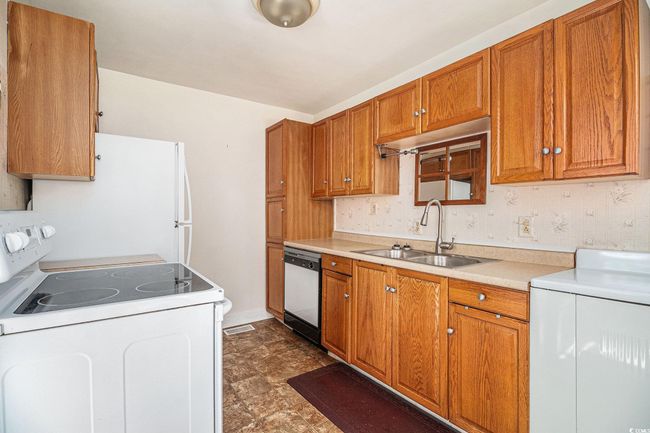 Kitchen with white appliances, washer / dryer, brown cabinetry, and light countertops | Image 10