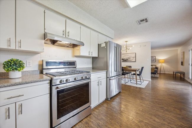 Kitchen featuring stainless steel appliances, under cabinet range hood, dark wood-style flooring, a textured ceiling, and white cabinetry | Image 11