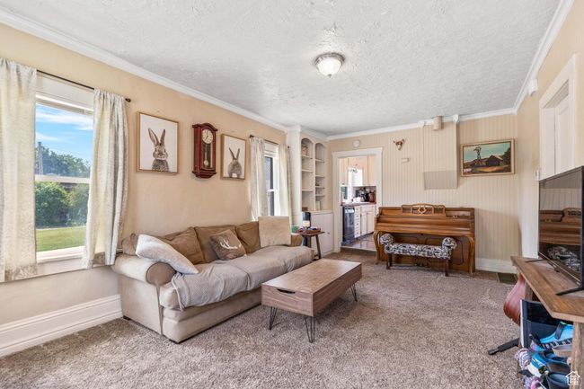 Living area with a textured ceiling, crown molding, carpet, and baseboards | Image 5